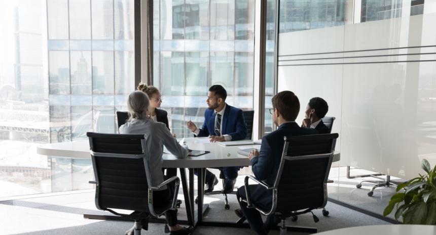 workers sitting around conference table in office with windows that show more offices