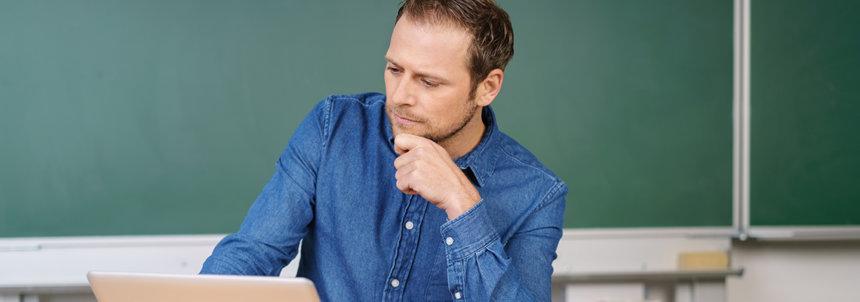 Male teacher sitting at desk staring pensively at laptop
