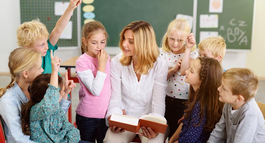 Elementary school teacher asking students a questions in classroom with kids raising their hands