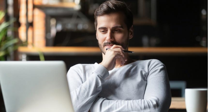 Man thinking with a pen in his hand and in front of his laptop